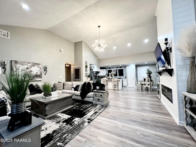 living room with an inviting chandelier, a large fireplace, high vaulted ceiling, and hardwood / wood-style floors