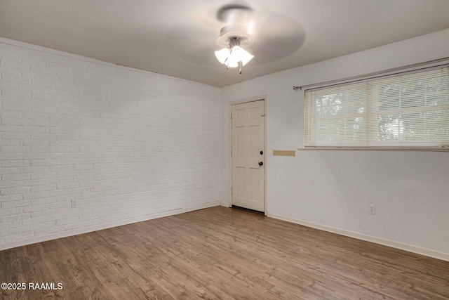 empty room featuring hardwood / wood-style flooring, brick wall, and ceiling fan