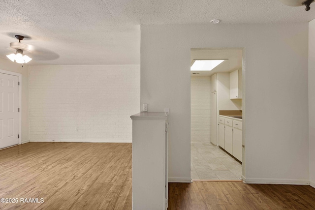 interior space featuring a textured ceiling, light hardwood / wood-style floors, ceiling fan, and brick wall