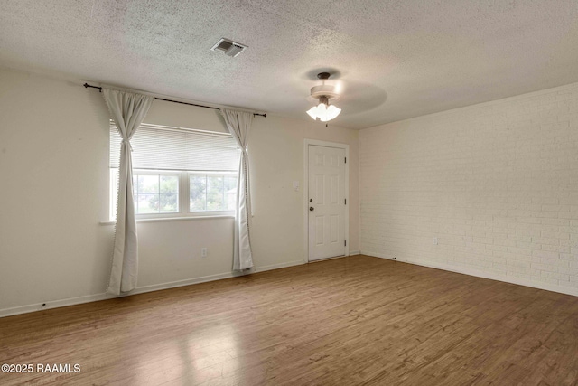 unfurnished room featuring hardwood / wood-style flooring, ceiling fan, brick wall, and a textured ceiling