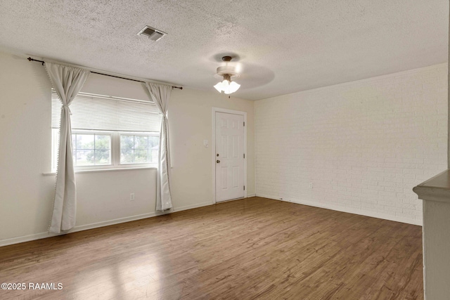 empty room with ceiling fan, brick wall, wood-type flooring, and a textured ceiling