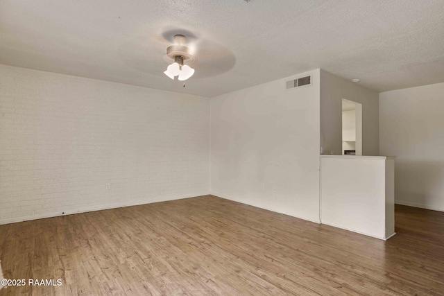 unfurnished room featuring hardwood / wood-style flooring, ceiling fan, brick wall, and a textured ceiling