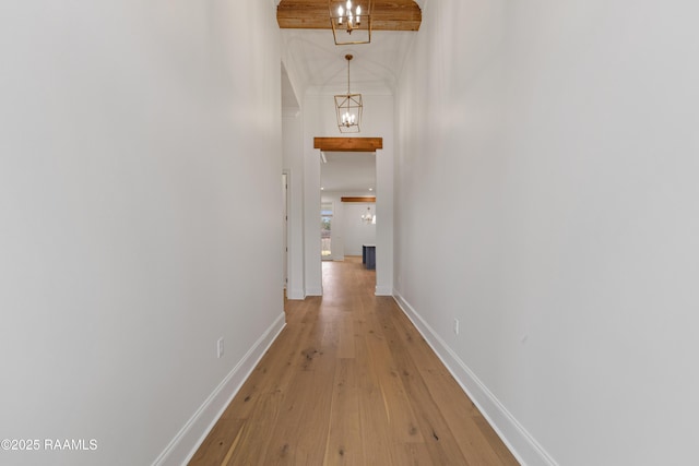 corridor featuring light wood-type flooring, an inviting chandelier, and a towering ceiling