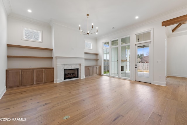 unfurnished living room featuring an inviting chandelier, ornamental molding, a high end fireplace, and light wood-type flooring