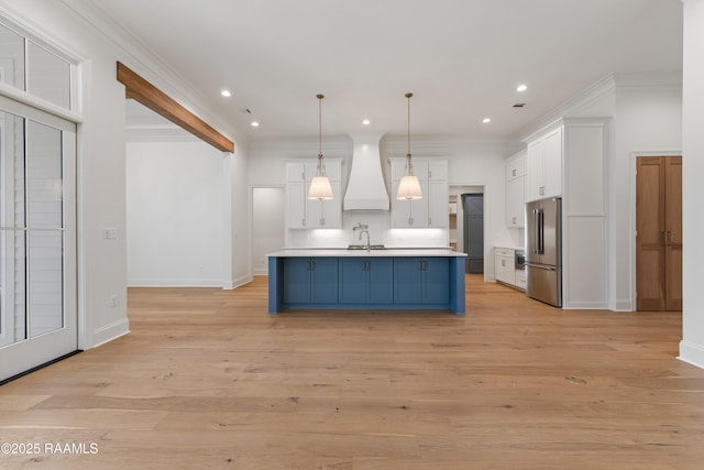 kitchen with decorative light fixtures, blue cabinets, an island with sink, high end fridge, and custom range hood