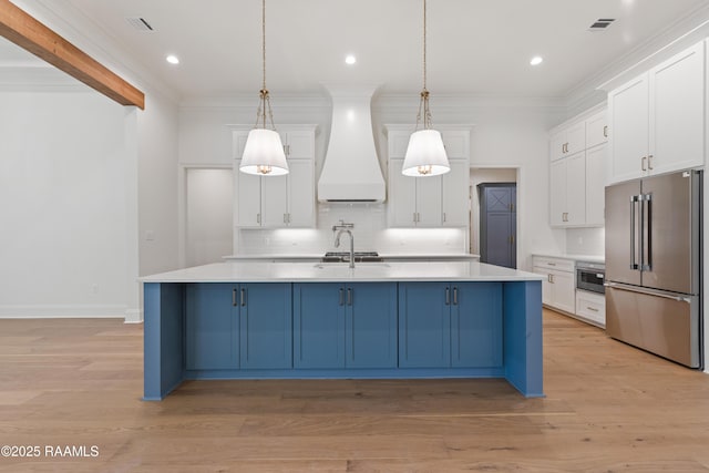 kitchen featuring white cabinetry, high end refrigerator, decorative light fixtures, custom range hood, and a kitchen island with sink