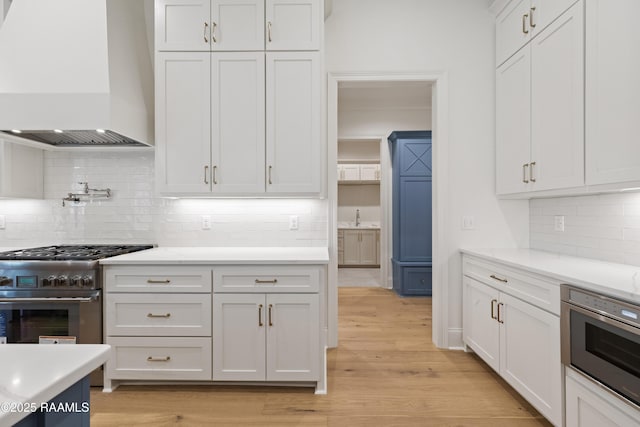 kitchen featuring light hardwood / wood-style flooring, white cabinetry, backsplash, stainless steel appliances, and wall chimney exhaust hood