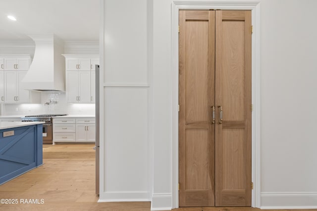 interior space with custom exhaust hood, white cabinetry, tasteful backsplash, high end range, and light hardwood / wood-style floors