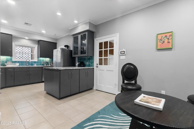 kitchen featuring sink, crown molding, light tile patterned floors, stainless steel refrigerator, and backsplash