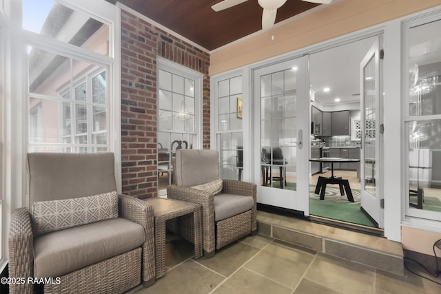 living area with ceiling fan and brick wall