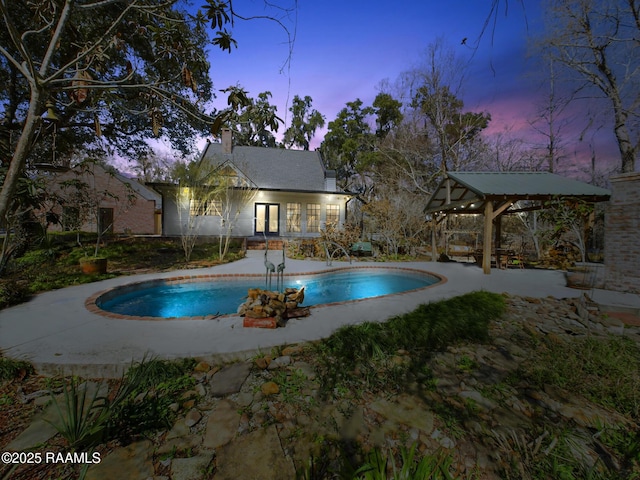 pool at dusk featuring an outbuilding and a gazebo