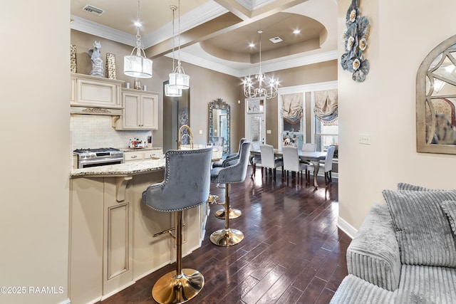 kitchen featuring gas range, dark hardwood / wood-style flooring, pendant lighting, light stone countertops, and cream cabinets