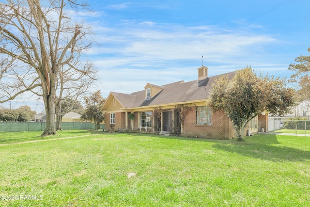 back of property with a chimney, fence, a lawn, and brick siding