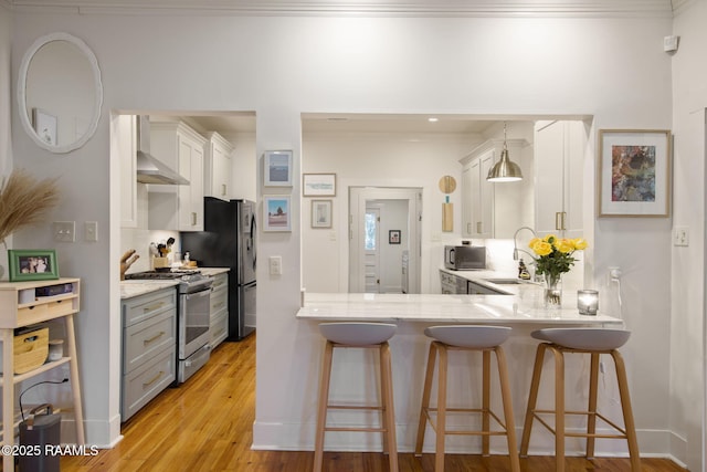 kitchen featuring wall chimney exhaust hood, sink, hanging light fixtures, stainless steel appliances, and white cabinets