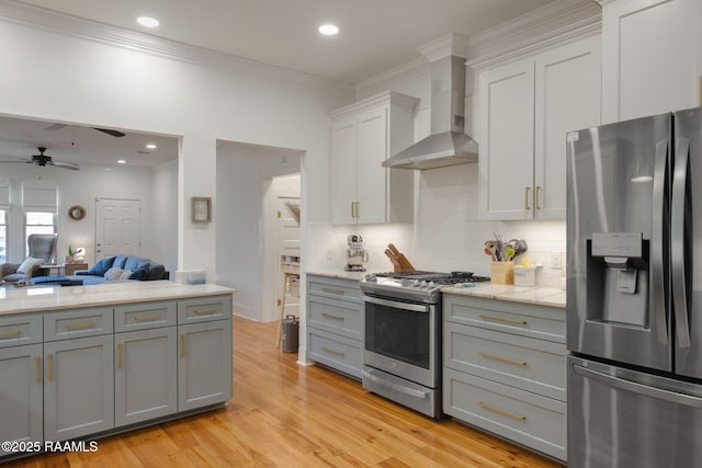 kitchen with gray cabinetry, appliances with stainless steel finishes, wall chimney range hood, light hardwood / wood-style floors, and white cabinets