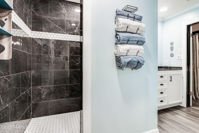 bathroom featuring hardwood / wood-style flooring, ornamental molding, a tile shower, and vanity