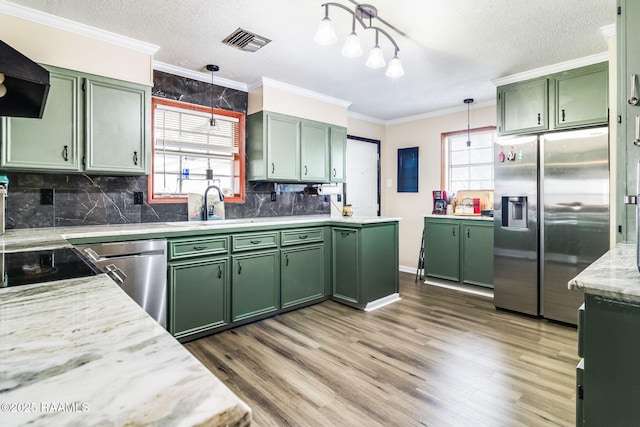 kitchen featuring sink, appliances with stainless steel finishes, green cabinets, hanging light fixtures, and exhaust hood