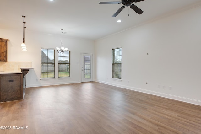 unfurnished living room with ceiling fan with notable chandelier, wood-type flooring, and ornamental molding