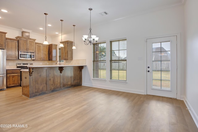 kitchen featuring appliances with stainless steel finishes, a breakfast bar area, hanging light fixtures, light hardwood / wood-style floors, and kitchen peninsula