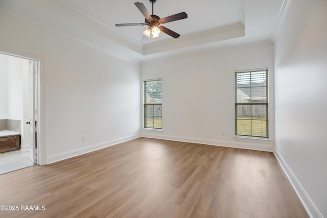 empty room featuring ornamental molding, a tray ceiling, light wood-type flooring, and a wealth of natural light