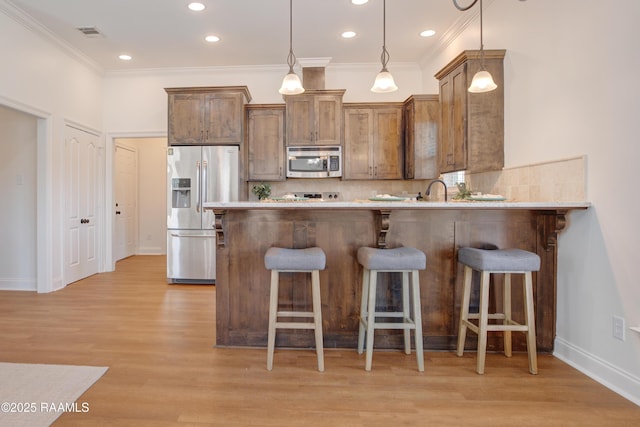 kitchen featuring appliances with stainless steel finishes, decorative light fixtures, backsplash, a kitchen bar, and kitchen peninsula