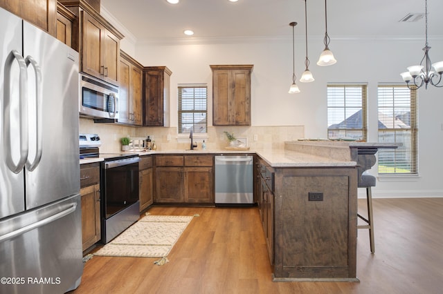 kitchen featuring a breakfast bar area, decorative light fixtures, appliances with stainless steel finishes, kitchen peninsula, and decorative backsplash