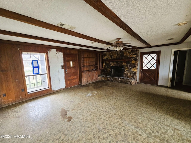 unfurnished living room with beam ceiling, a textured ceiling, and wood walls