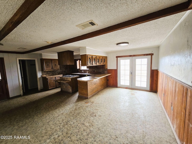 kitchen featuring french doors, a textured ceiling, beam ceiling, and wood walls