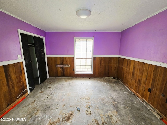 spare room featuring concrete floors, a textured ceiling, and wood walls