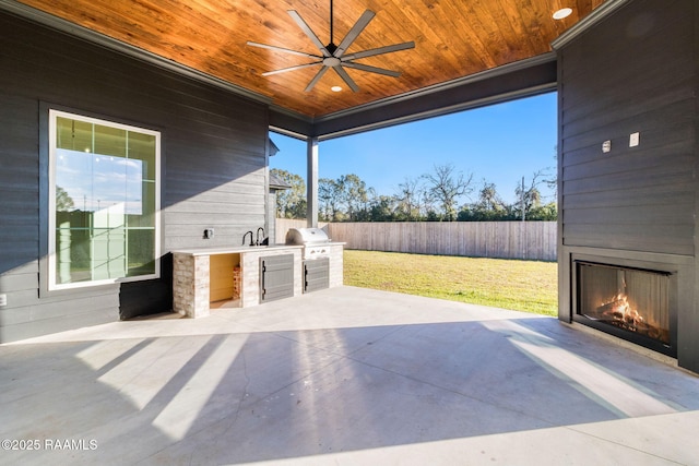 view of patio featuring a fireplace, ceiling fan, and an outdoor kitchen