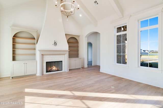 unfurnished living room with beamed ceiling, built in features, a fireplace, and light hardwood / wood-style flooring