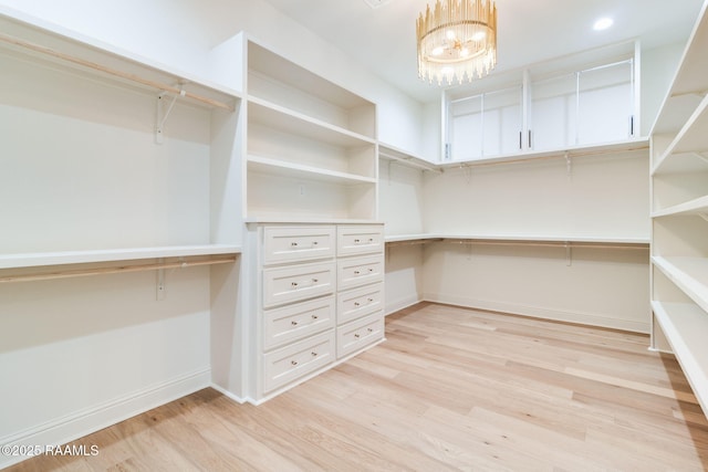 spacious closet with an inviting chandelier, built in desk, and light hardwood / wood-style floors