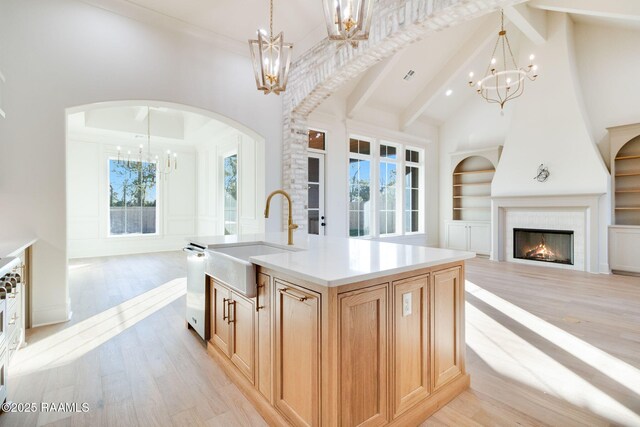 kitchen featuring built in shelves, sink, a notable chandelier, a fireplace, and a kitchen island with sink