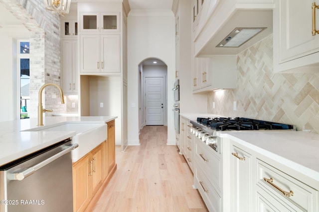 kitchen featuring premium range hood, sink, white cabinets, stainless steel appliances, and light wood-type flooring