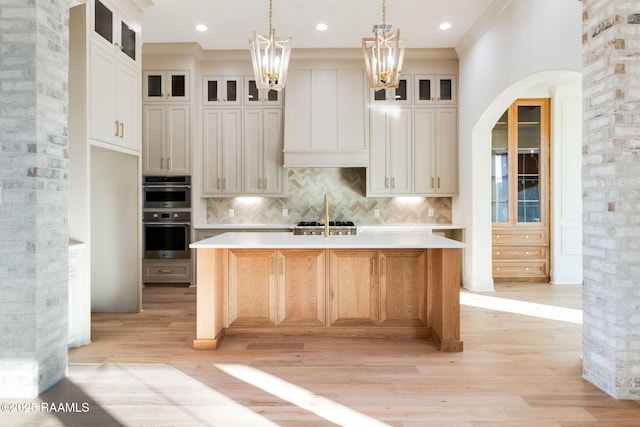 kitchen with a spacious island, tasteful backsplash, decorative light fixtures, light wood-type flooring, and stainless steel double oven