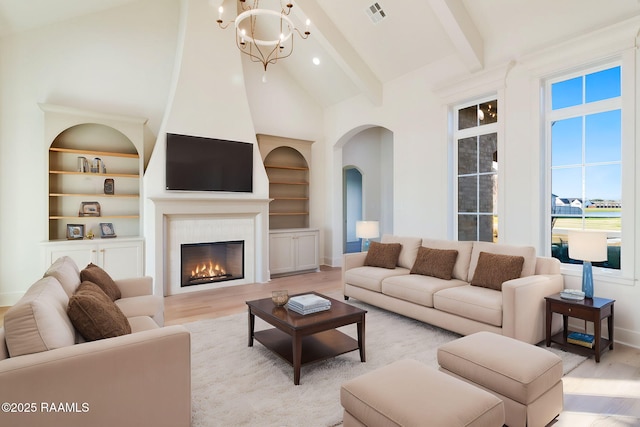 living room featuring beamed ceiling, an inviting chandelier, built in features, and light hardwood / wood-style flooring