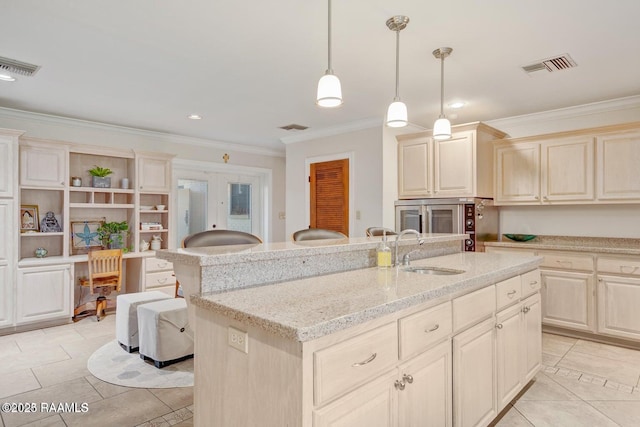 kitchen with sink, crown molding, hanging light fixtures, light stone countertops, and a center island with sink