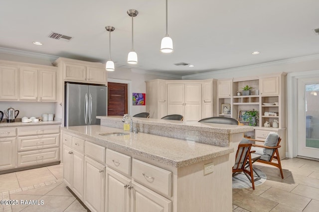 kitchen with hanging light fixtures, a kitchen island with sink, sink, and stainless steel fridge