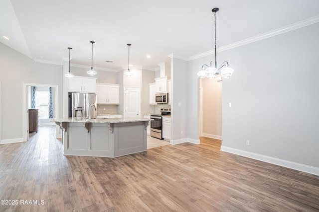 kitchen with decorative light fixtures, white cabinetry, a large island with sink, stainless steel appliances, and light hardwood / wood-style flooring