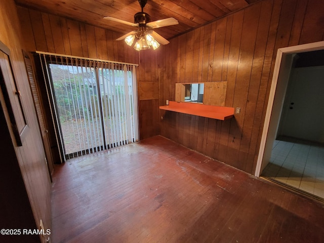 empty room with wood-type flooring, ceiling fan, wood ceiling, and wood walls