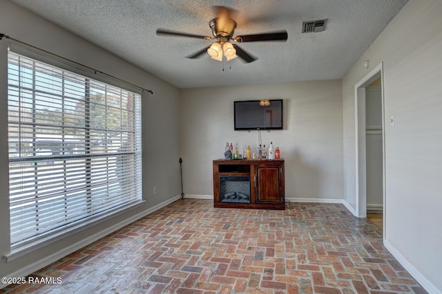 unfurnished living room featuring ceiling fan and a textured ceiling