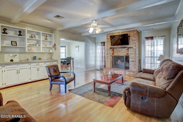 living room with beam ceiling, a fireplace, a textured ceiling, and light hardwood / wood-style floors