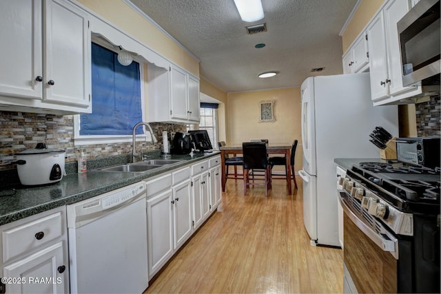 kitchen with sink, backsplash, white cabinets, stainless steel appliances, and light wood-type flooring