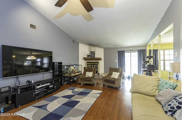 living room with vaulted ceiling, ceiling fan, a brick fireplace, dark wood-type flooring, and a textured ceiling