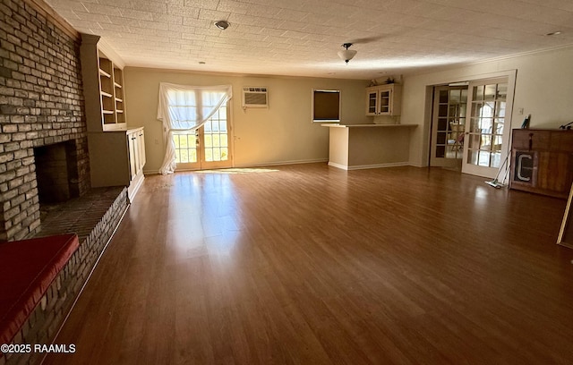 unfurnished living room featuring dark wood-type flooring, french doors, ornamental molding, a wall unit AC, and a fireplace