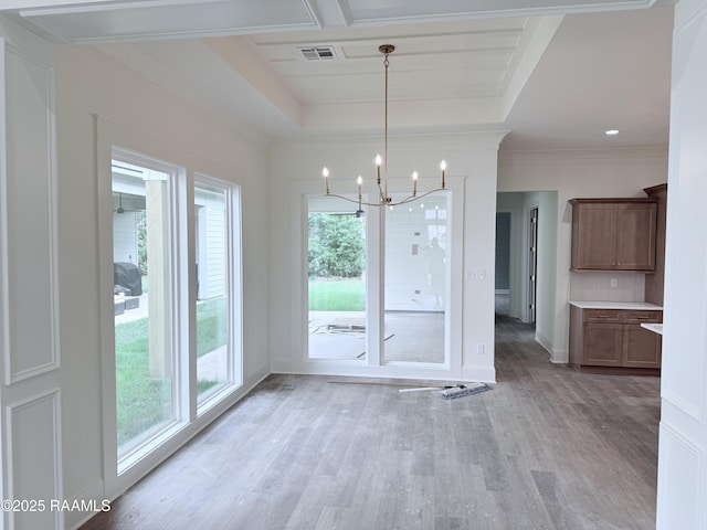 unfurnished dining area featuring a chandelier, light wood-type flooring, a tray ceiling, baseboards, and visible vents
