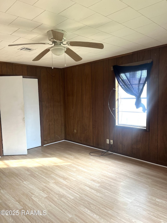 spare room featuring ceiling fan, wooden walls, and light wood-type flooring