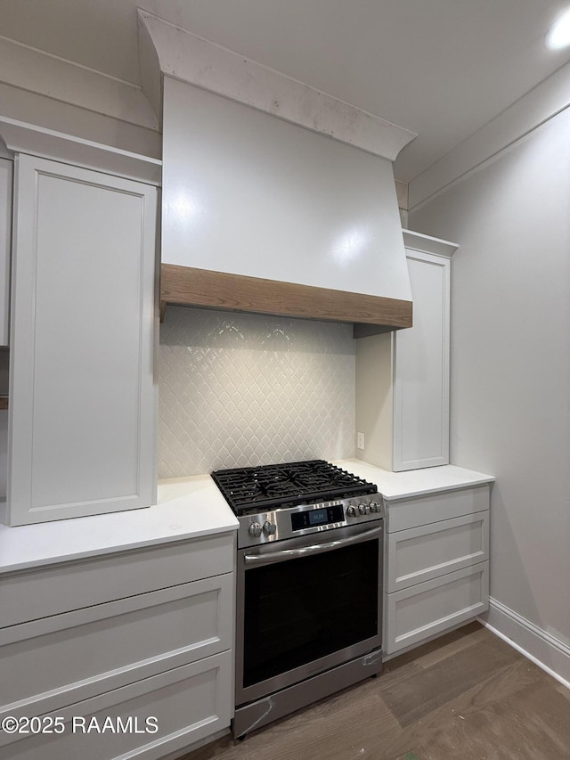 kitchen featuring stainless steel gas stove, white cabinetry, dark hardwood / wood-style floors, custom range hood, and backsplash