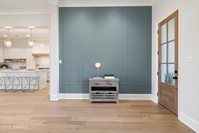 entryway with crown molding, plenty of natural light, light wood-type flooring, and a decorative wall