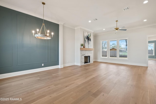 unfurnished living room with ceiling fan with notable chandelier, a fireplace, visible vents, light wood finished floors, and crown molding